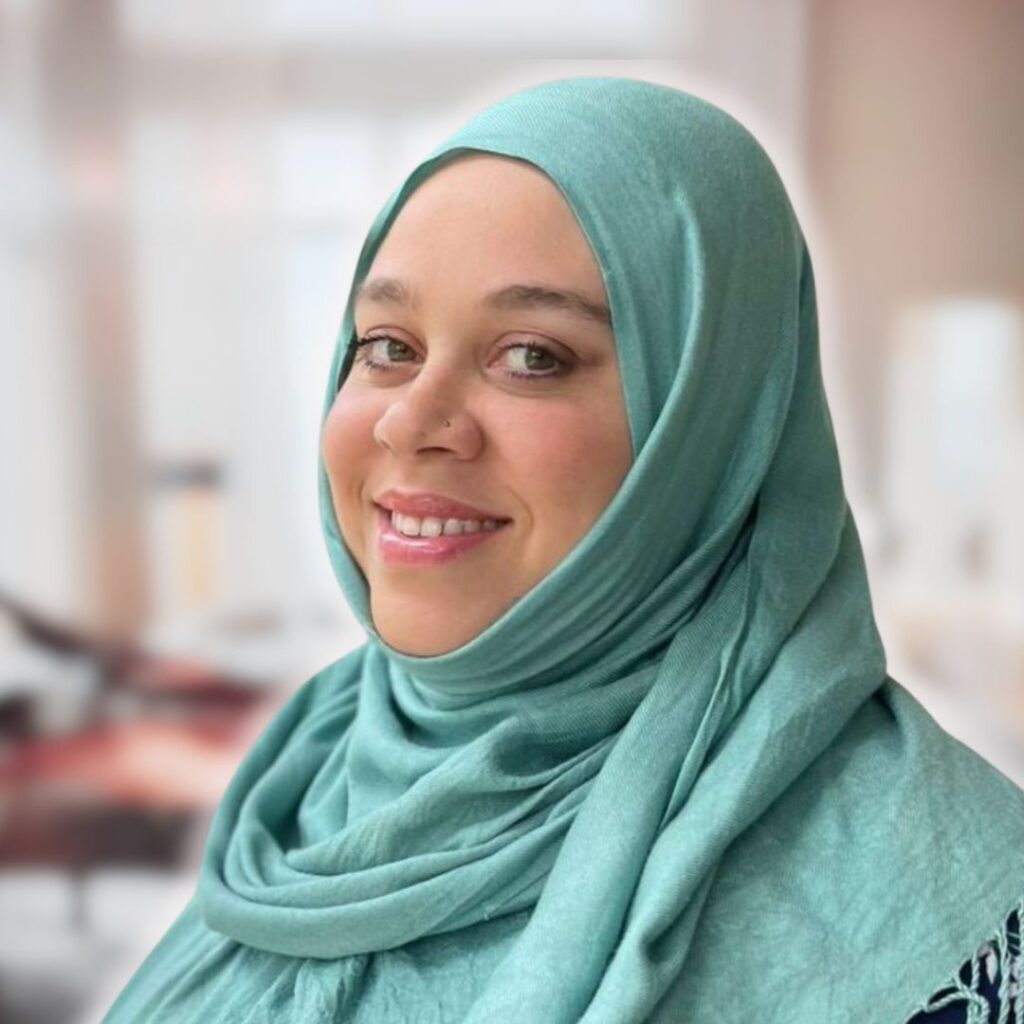 Smiling woman wearing a teal hijab, representing intuitive life coaching and personal growth, with a soft background suggesting a supportive environment.