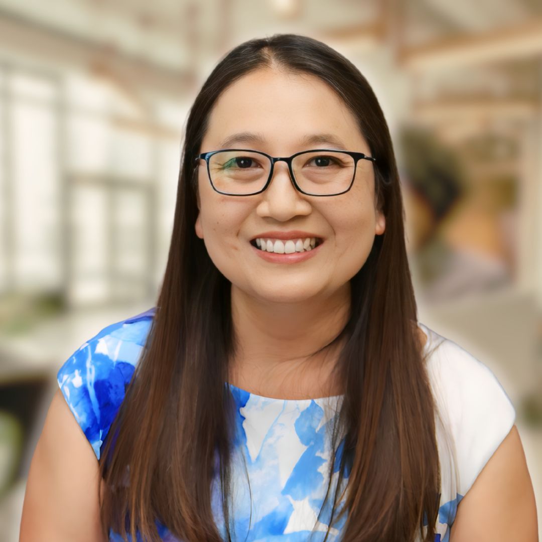 Smiling woman in a blue and white dress, representing empowerment and transformation in coaching, set in a professional environment.