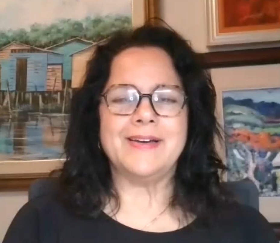 Smiling woman with glasses in front of colorful artwork, representing a supportive community in coaching and mentorship at Elevate.